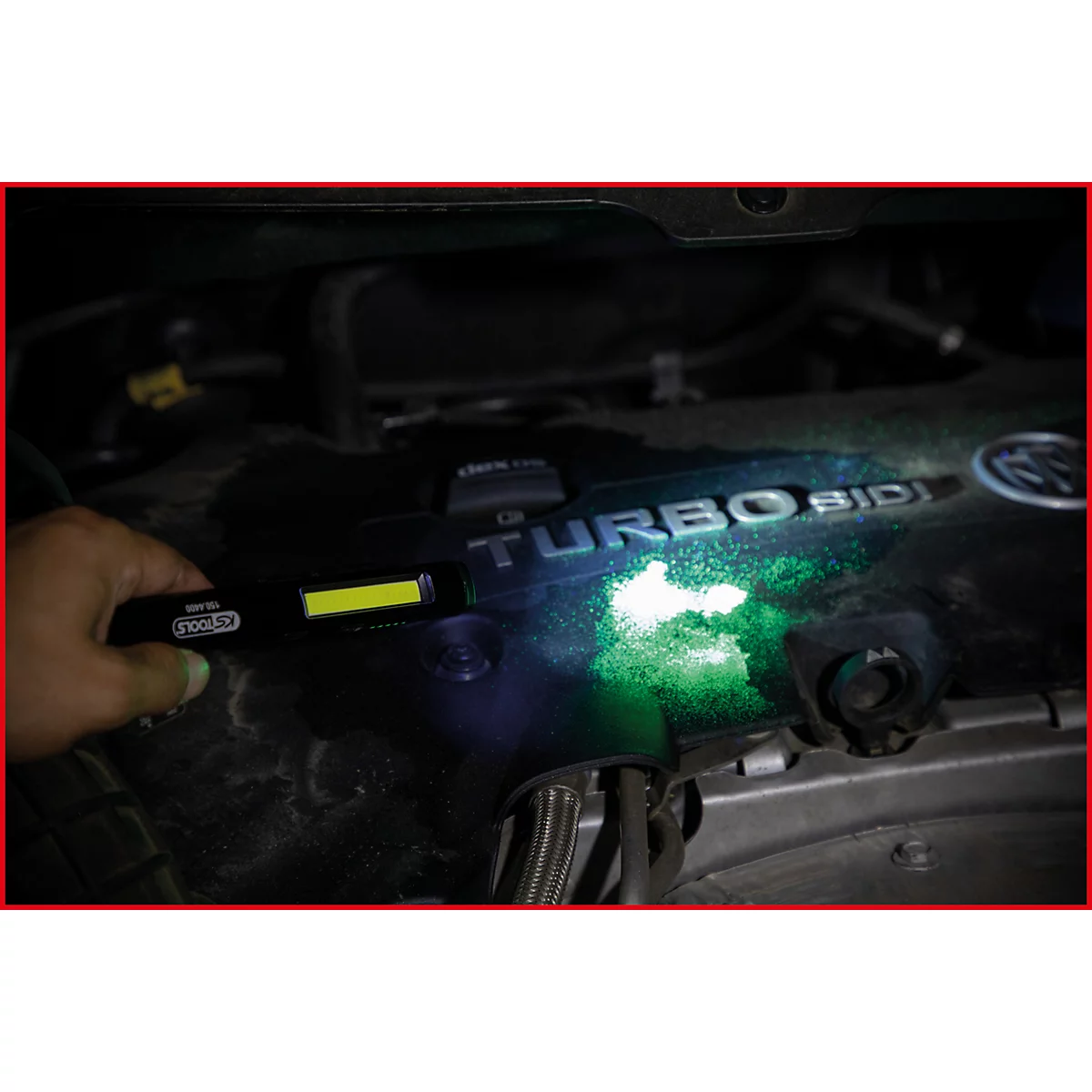 Een hand houdt een werkplaatslamp boven een motor. De motor gloeit groen in het licht, de tekst "TURBO SIDI" is te zien.